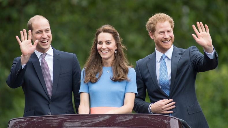 Kate Middleton in a light blue dress in between Prince William and Prince Harry.